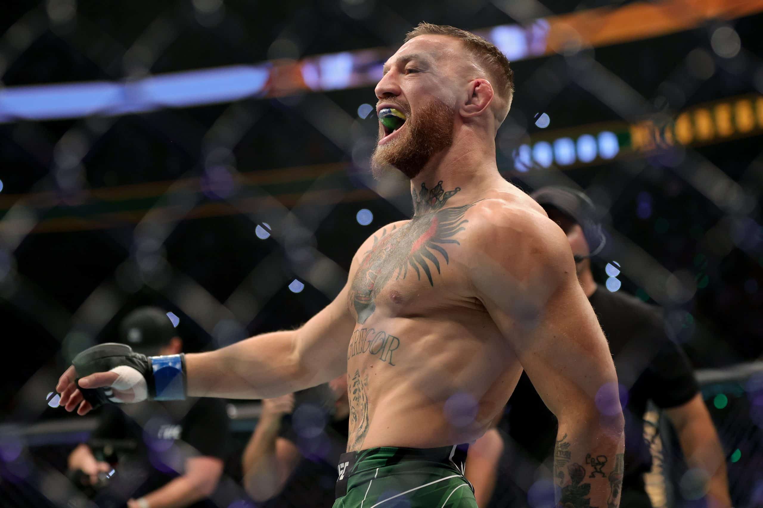 Conor McGregor sem camisa, usando protetor bucal e proteção nas mãos, dentro de octógono para luta do UFC